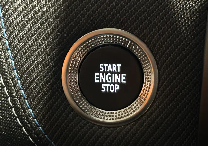 Gros plan sur le bouton Start Engine Stop entouré d’un cerclage métallique et d’un habillage noir avec surpiqûres bleues.