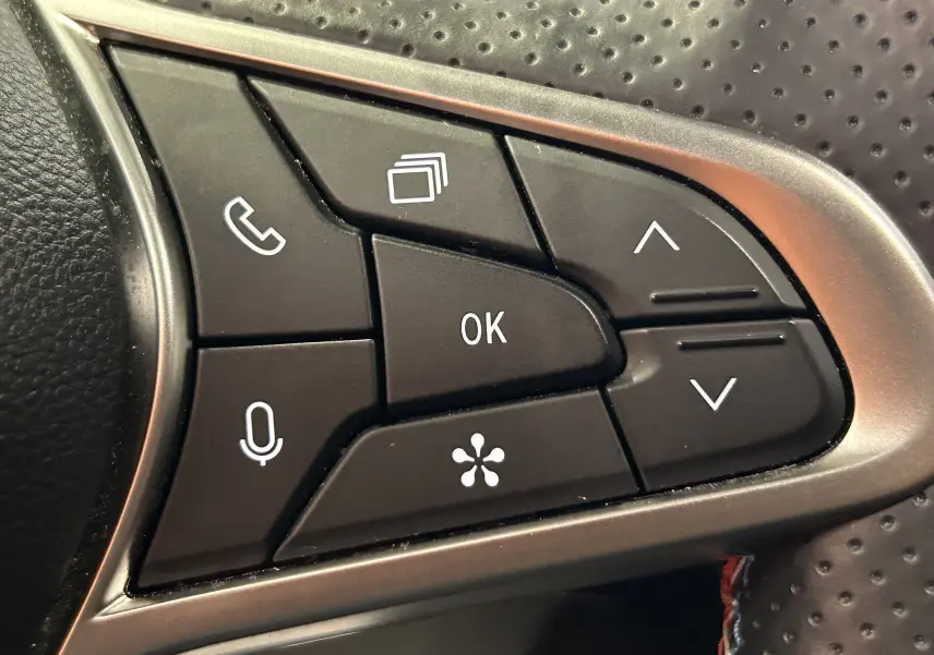 Gros plan sur les commandes multifonctions noires du volant perforé du Renault Captur bleu Iron, version hybride 2025.