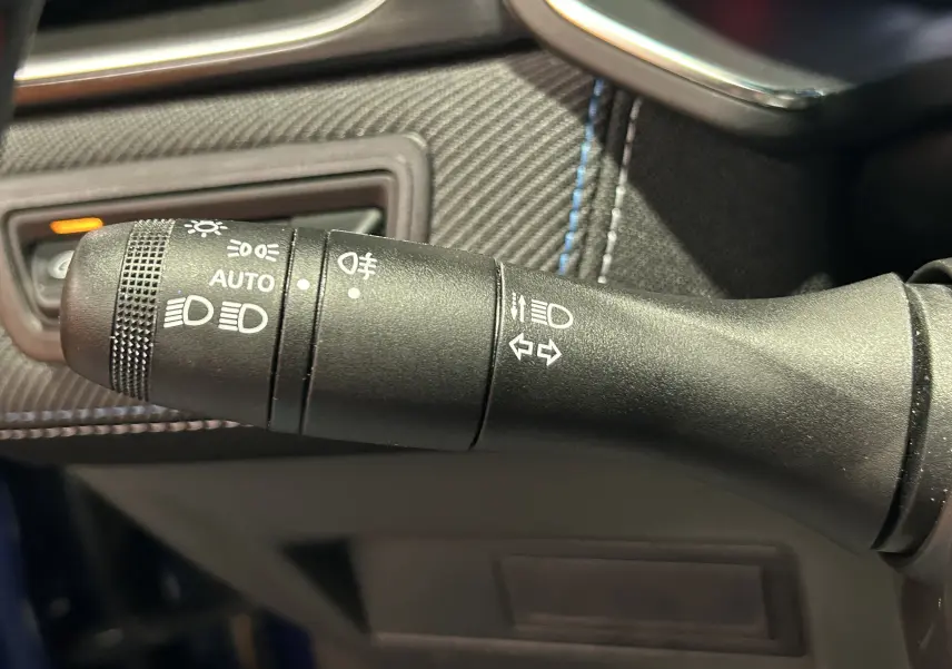 Gros plan sur la commande des phares et clignotants du Renault Captur bleu Iron, avec détails des symboles lumineux.