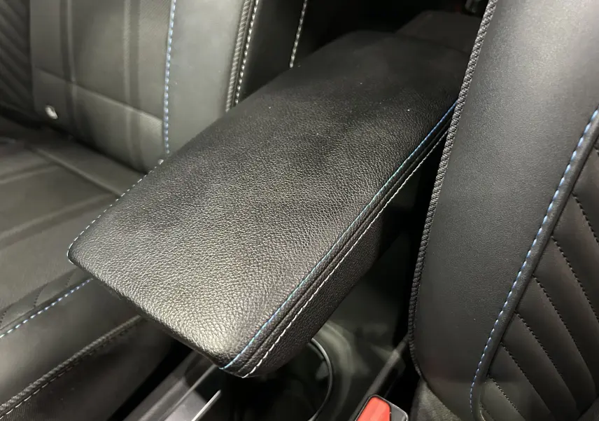 Détail de l'accoudoir central en cuir noir avec surpiqûres bleues sur les sièges avant du Renault Captur II Ph.2.