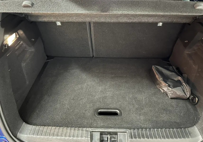 Coffre ouvert vu de face d’un Renault Captur bleu Iron, avec tapis noir et sac de rangement sur le côté droit.