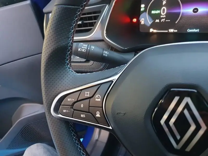 Gros plan sur le volant cuir multifonction noir avec logo Renault et commandes de régulateur sur la gauche, intérieur bleu Iron visible.