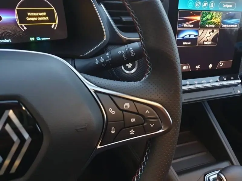 Gros plan sur le volant cuir perforé et les commandes multifonctions du Renault Captur 2025, écran tactile en arrière-plan.