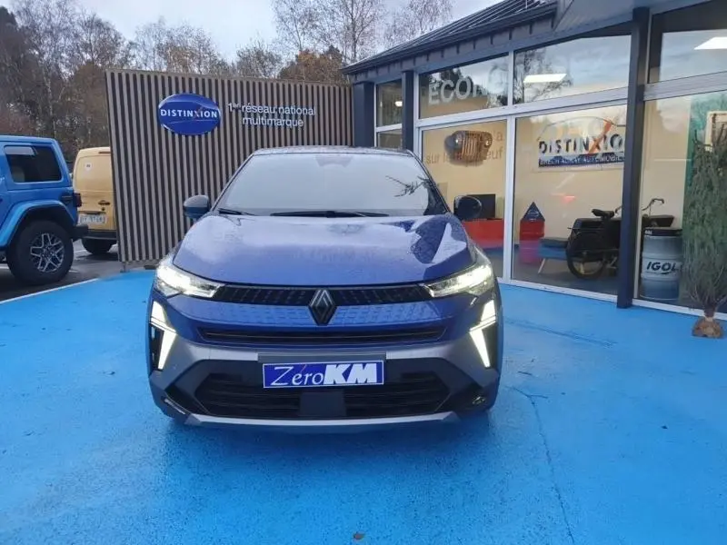 Vue avant d'un Renault Captur 2025 Bleu Iron avec feux LED allumés sur un sol bleu devant un showroom.