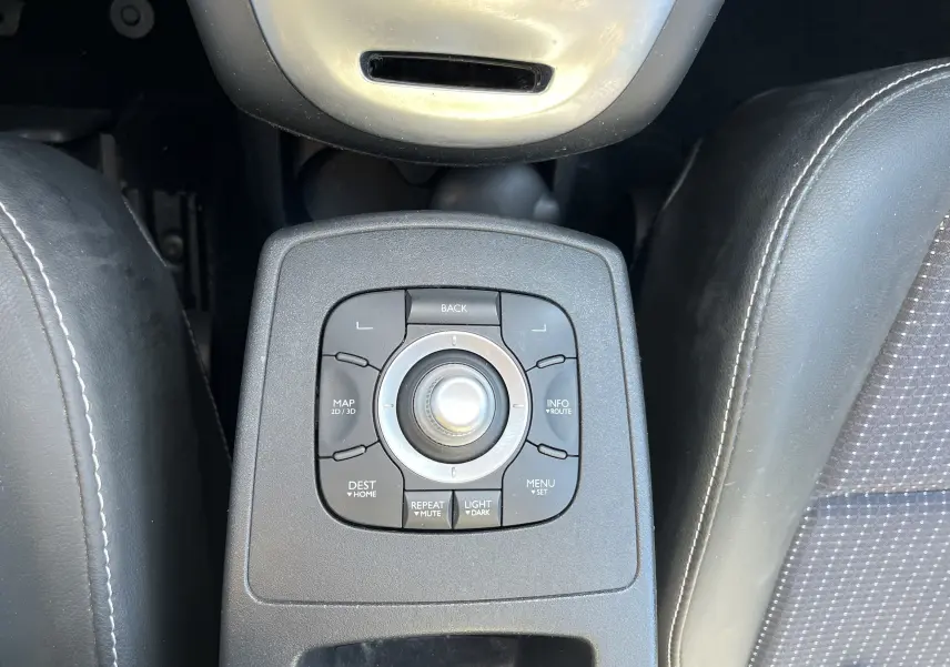 Gros plan sur la commande centrale du système multimédia du Renault Scenic III noir, avec boutons de navigation et molette.