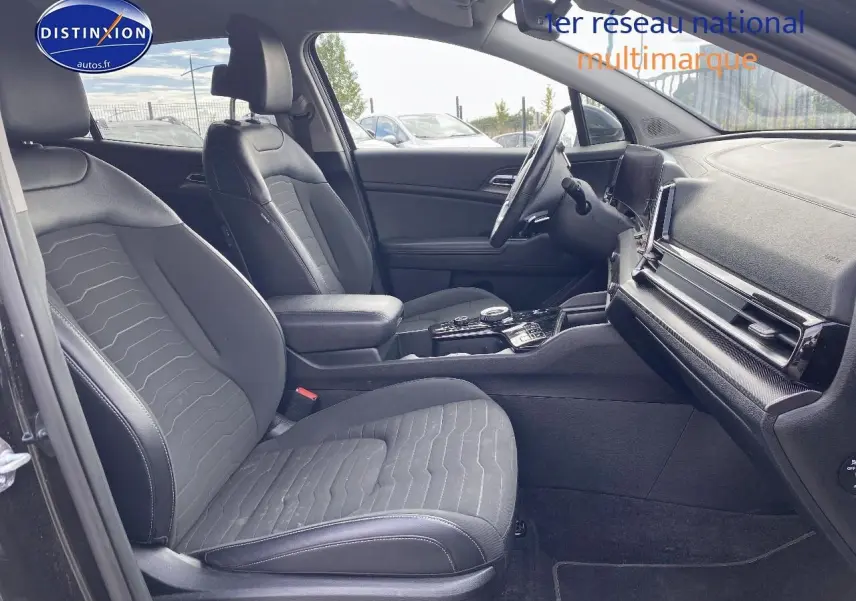 Intérieur avant du KIA SPORTAGE 2023 noir, sièges tissu noir, console centrale avec écran tactile et volant multifonction.