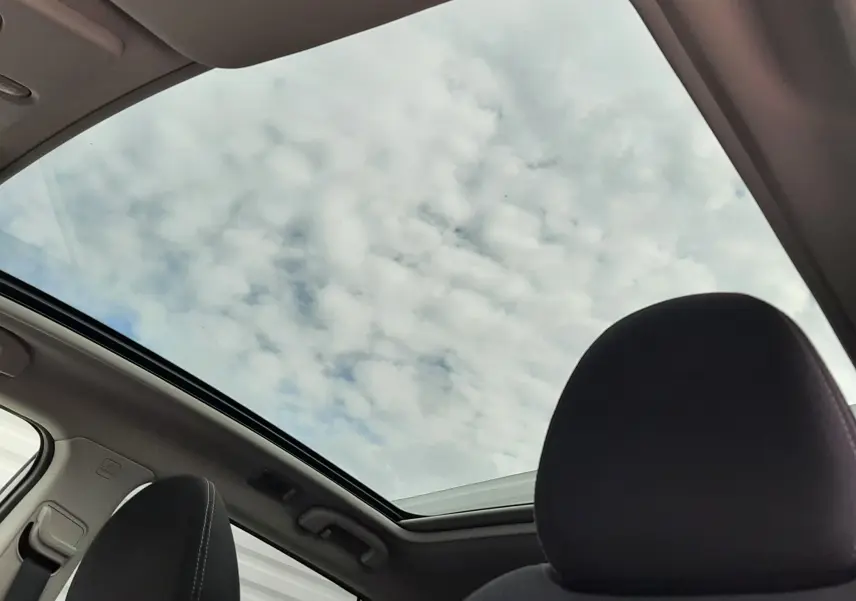 Toit panoramique ouvert vu de l'intérieur avant du Nissan Qashqai blanc, avec sièges noirs en tissu.