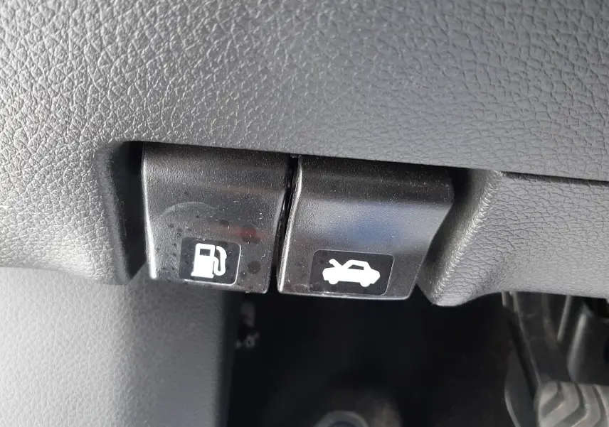 Gros plan sur les leviers d'ouverture du capot et de la trappe à carburant dans l'habitacle d'un Nissan Qashqai blanc.
