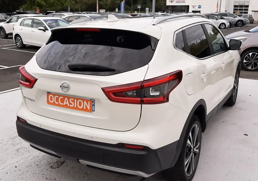 Vue 3/4 arrière droite d'un Nissan Qashqai blanc 2020 avec vitres teintées et toit équipé de barres de toit.