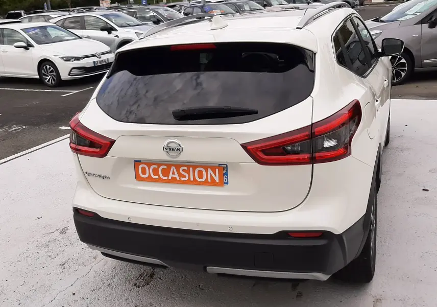Vue 3/4 arrière d'un Nissan Qashqai blanc 2020 avec vitres teintées et plaque "OCCASION" orange.