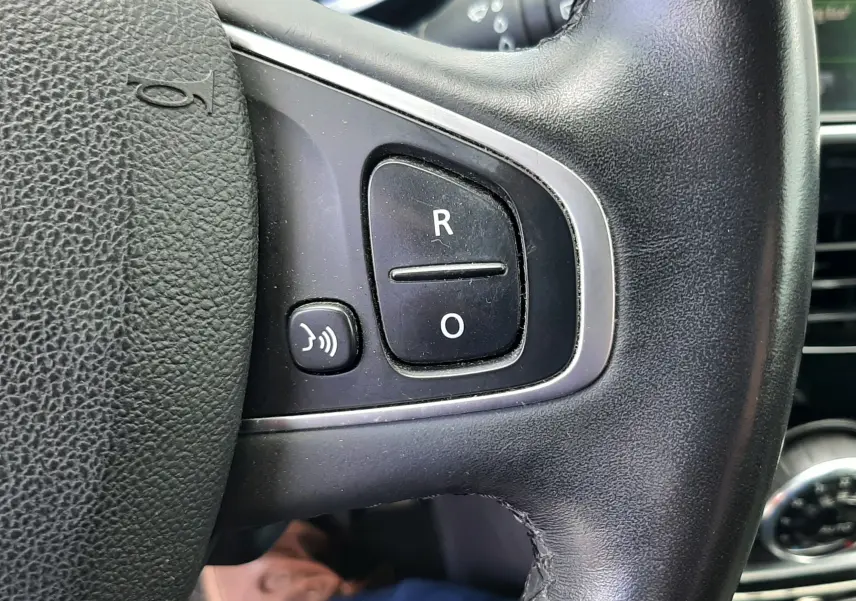 Gros plan sur les commandes du volant en cuir noir d'une Renault Clio IV Estate beige, avec boutons R et O visibles.