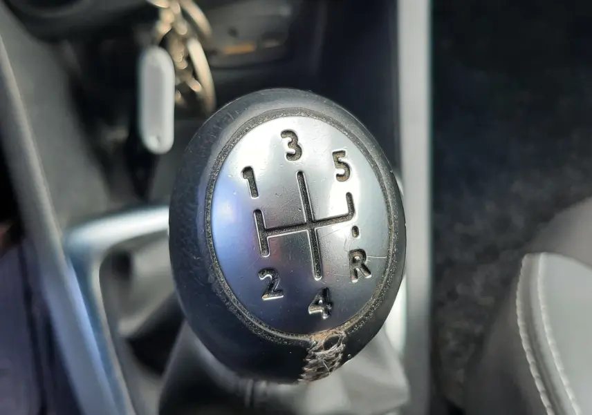 Gros plan sur le levier de vitesse manuel noir et argenté de la Renault Clio IV Estate beige, intérieur tissu noir.