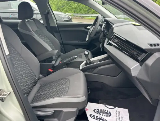 Vue intérieure côté gauche de l'Audi A1 Sportback 2025 gris, sièges sport, volant cuir et console centrale avec boîte manuelle.
