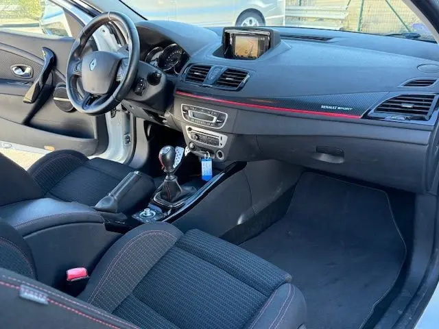 Intérieur de la Renault Mégane III Coupé 2.0T RS blanc nacré, vue côté conducteur, tableau de bord avec écran et levier manuel.
