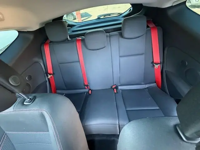 Vue intérieure arrière de la Renault Mégane III Coupé 2.0T RS avec sièges noirs et ceintures rouges contrastantes.