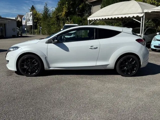 Profil côté gauche de la Renault Mégane III Coupé 2.0T RS blanc nacré avec jantes noires et lignes sportives marquées.