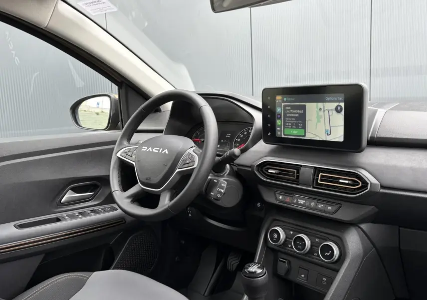 Vue intérieure côté conducteur de la Dacia Sandero Stepway 2025 beige avec volant multifonction et écran tactile GPS.