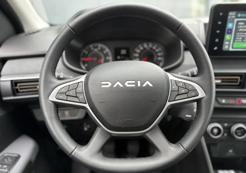 Vue rapprochée du volant noir Dacia avec commandes intégrées, tableau de bord et écran tactile du Sandero Stepway 2025.