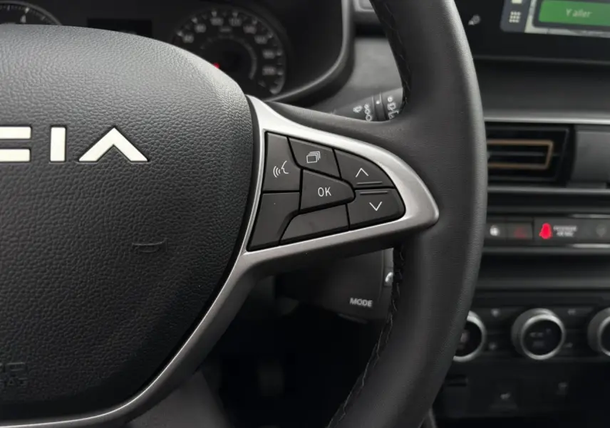Gros plan sur le volant noir de la Dacia Sandero Stepway 2025, avec commandes multifonctions et tableau de bord en arrière-plan.