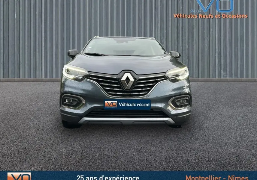 Vue frontale d'un Renault Kadjar gris 2019 avec feux allumés et calandre chromée sur fond industriel.
