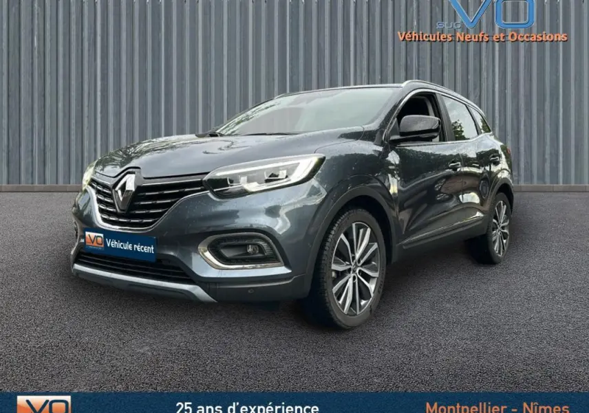 Renault Kadjar gris 3/4 avant droit avec jantes alliage 18 pouces et barres de toit visibles sur fond urbain.