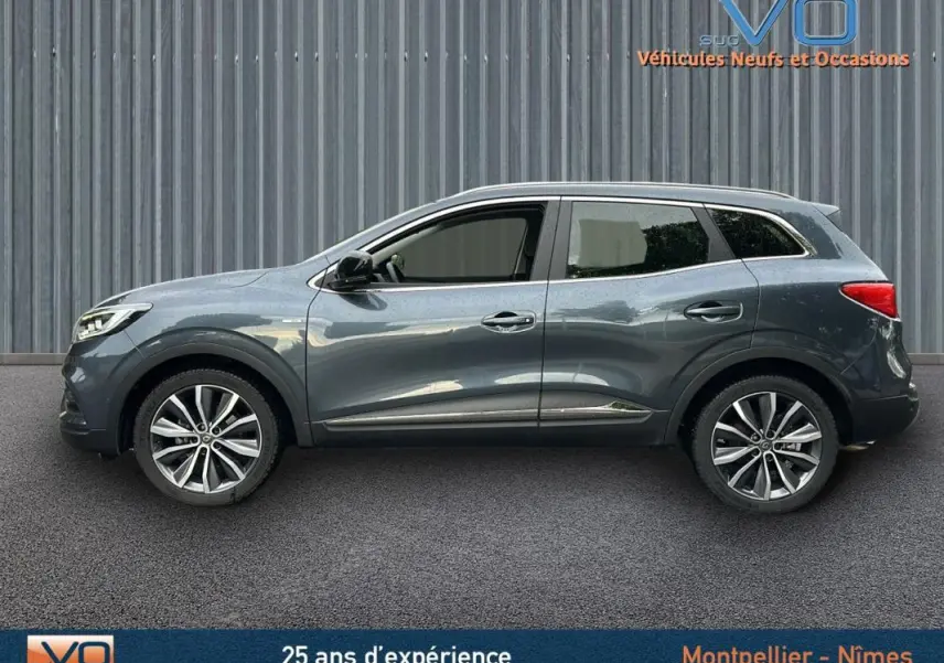 Profil côté gauche du Renault Kadjar gris 2019 avec jantes alliage 18 pouces et barres de toit visibles.