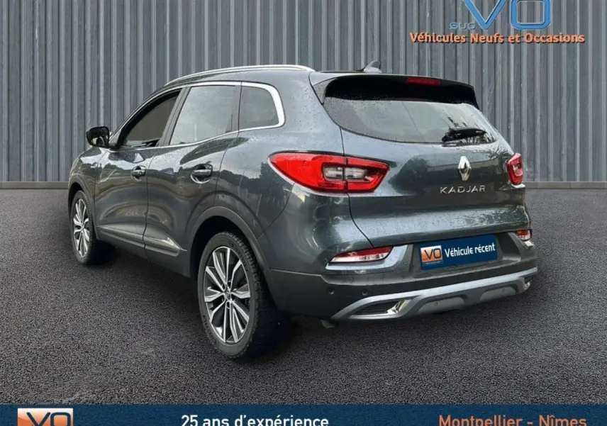 Vue 3/4 arrière droite d'un Renault Kadjar gris 2019 avec jantes alliage 18 pouces et barres de toit visibles.