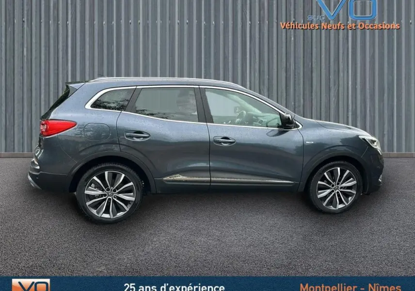 Profil côté droit du Renault Kadjar gris 2019 avec jantes alliage 18 pouces et barres de toit visibles.