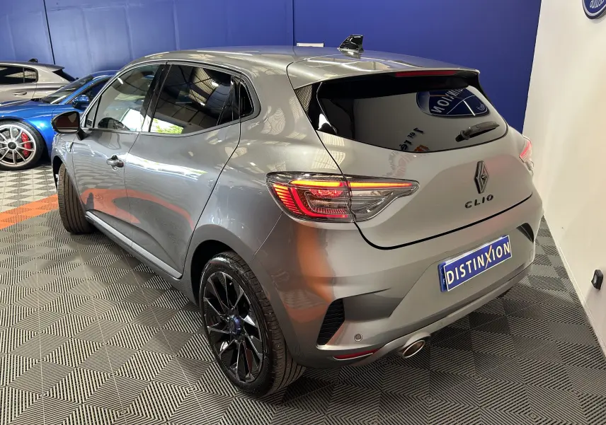 Vue 3/4 arrière droite d'une Renault Clio V TCe 90 Esprit Alpine gris schiste avec jantes noires et feux allumés.
