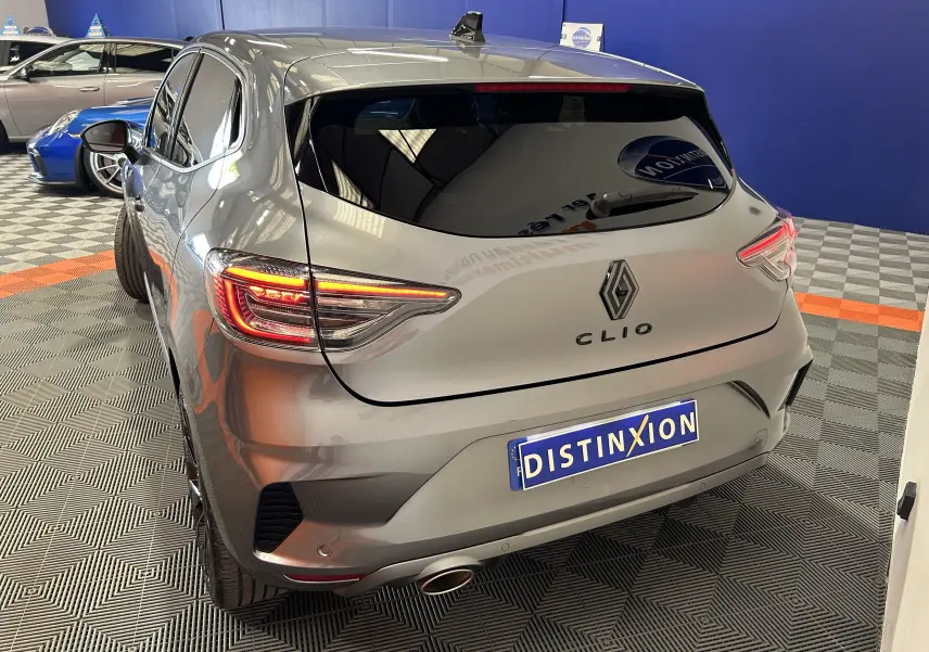 Vue 3/4 arrière droite d'une Renault Clio V gris schiste avec feux arrière allumés dans un showroom.