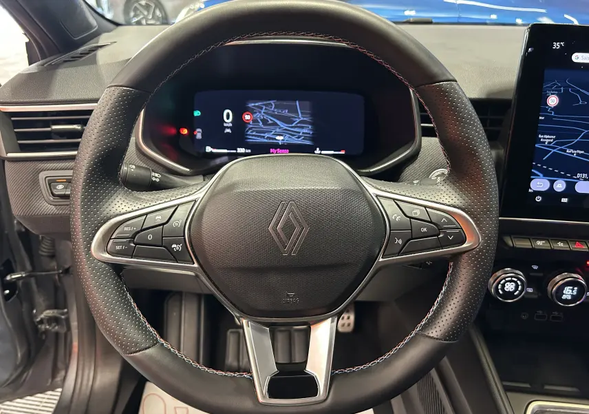 Vue intérieure centrée sur le volant noir perforé de la Renault Clio V TCe 90 Esprit Alpine avec tableau de bord digital.