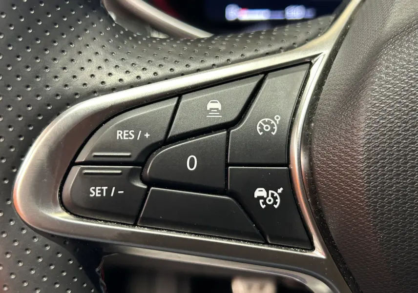 Gros plan sur les commandes de régulateur de vitesse au volant perforé d'une Renault Clio V gris schiste.