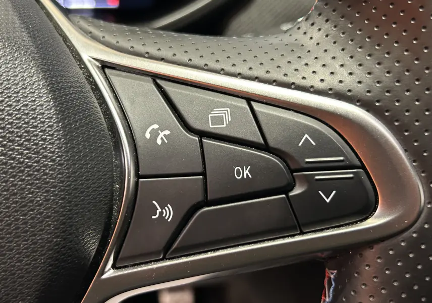 Gros plan sur les commandes multifonctions noires du volant perforé de la Renault Clio V TCe 90 Esprit Alpine gris schiste.