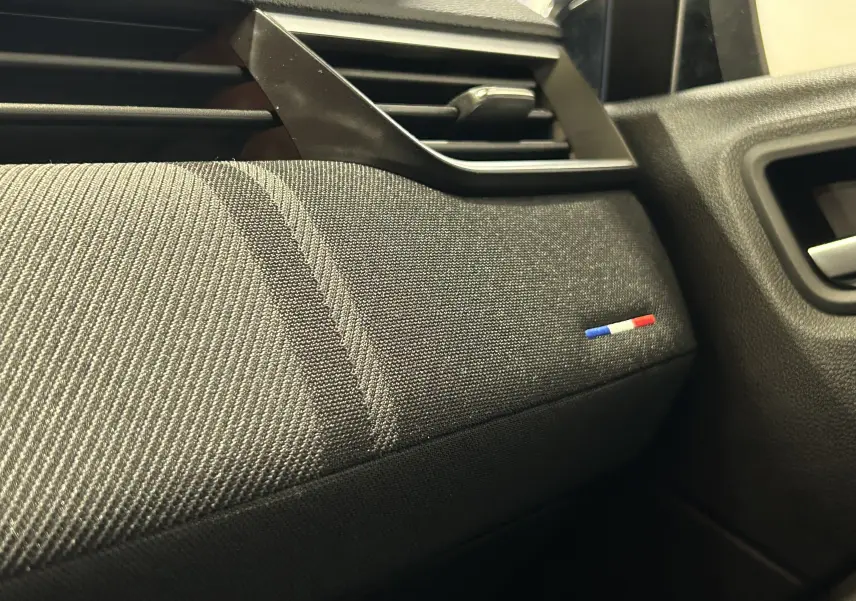 Gros plan sur la garniture intérieure côté passager de la Renault Clio V gris schiste avec détail du drapeau tricolore français.