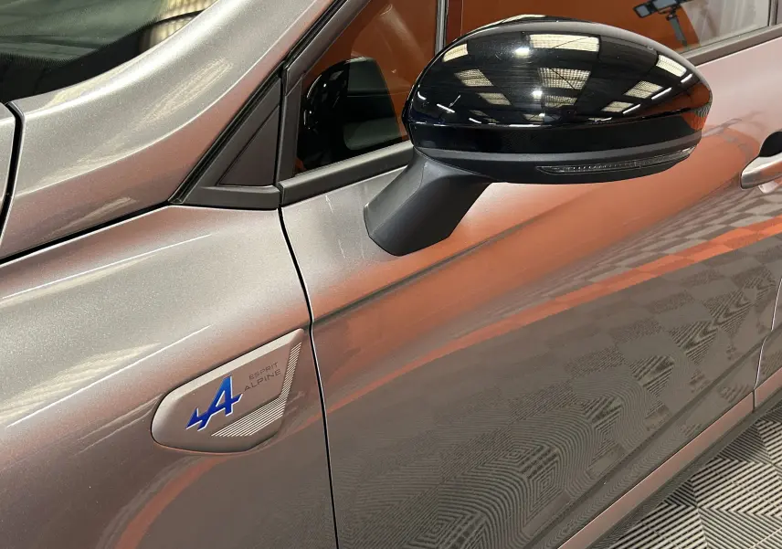 Détail du rétroviseur noir et logo Alpine bleu sur la porte côté gauche d'une Renault Clio V gris schiste.