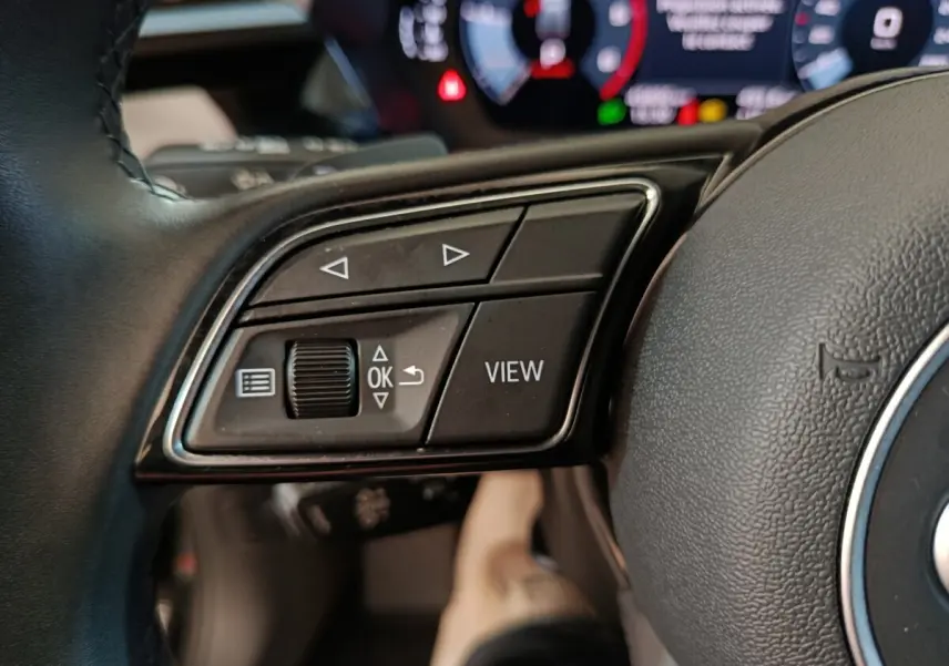 Gros plan sur les commandes gauche du volant cuir noir de l'Audi A3 35 TDI 2023 avec affichage digital en arrière-plan.