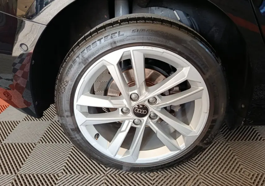 Gros plan sur la roue avant droite d'une Audi A3 noire, jante alliage argentée à cinq doubles branches.