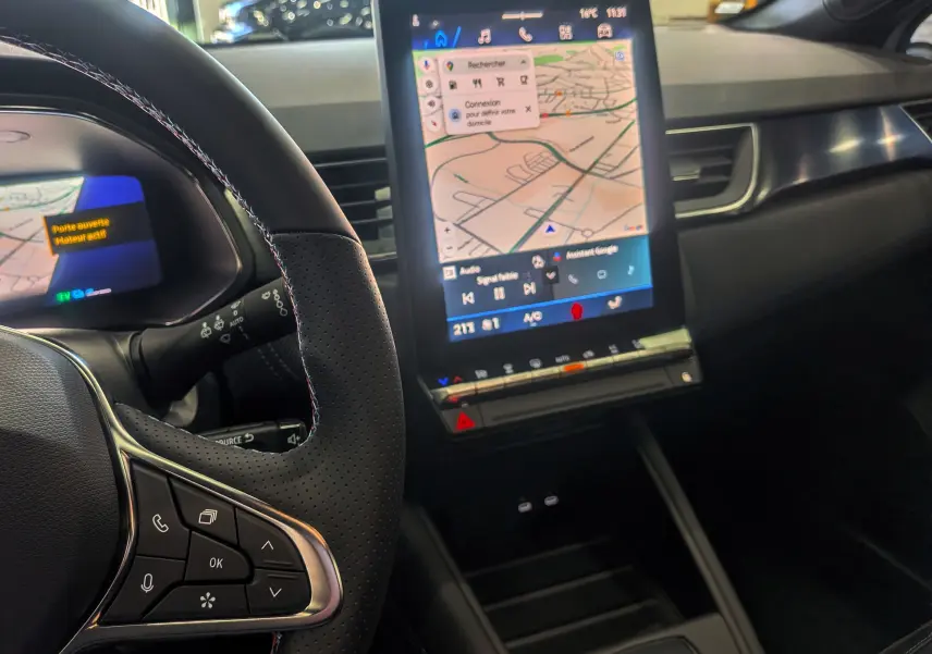 Vue intérieure centrée sur le volant et l'écran tactile vertical du tableau de bord du Renault Symbioz blanc nacré.