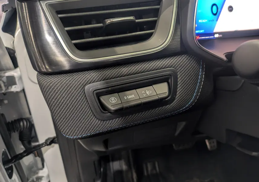 Détail intérieur côté gauche du tableau de bord du Renault Symbioz blanc nacré, avec commandes E-SAVE et réglage phares.