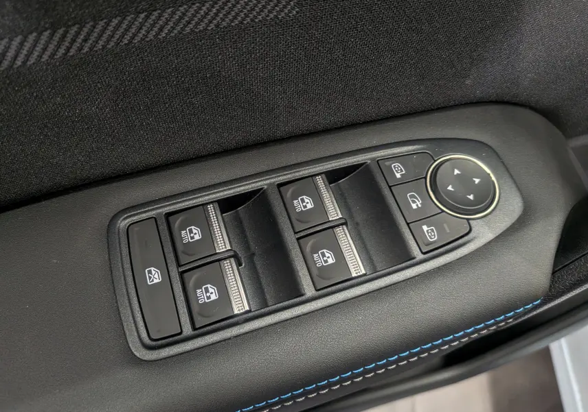 Gros plan sur les commandes de lève-vitres et rétroviseurs sur la porte côté gauche, intérieur noir avec surpiqûres bleues.