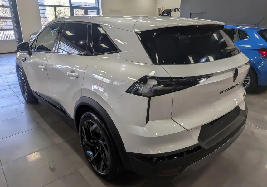 Vue 3/4 arrière droite du Renault SYMBIOZ blanc nacré avec vitres teintées et jantes noires en showroom.