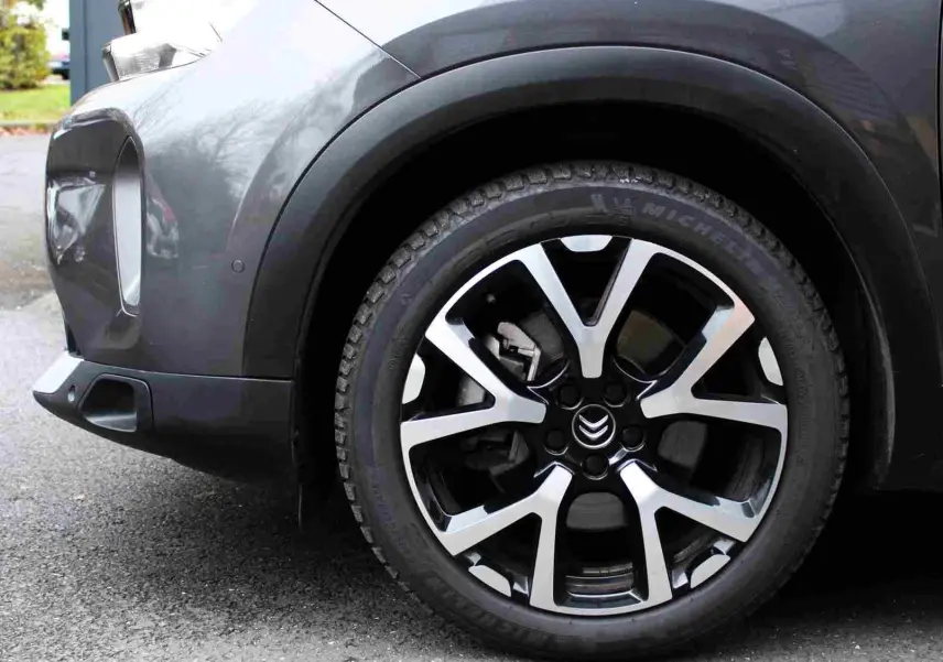 Gros plan sur la roue avant droite d’un Citroën C5 Aircross gris platinium avec jante alliage bicolore et logo Citroën.