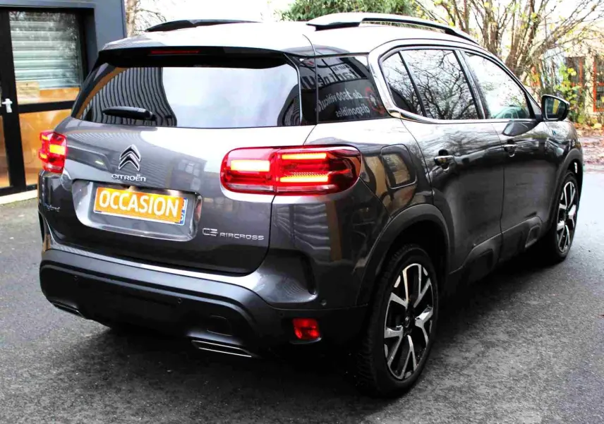 Vue 3/4 arrière droite d'un Citroën C5 Aircross gris platinium avec feux arrière allumés et jantes noires.