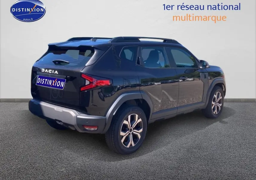 Vue 3/4 arrière droite du Dacia Duster noir 2025 avec jantes alu et barres de toit visibles.
