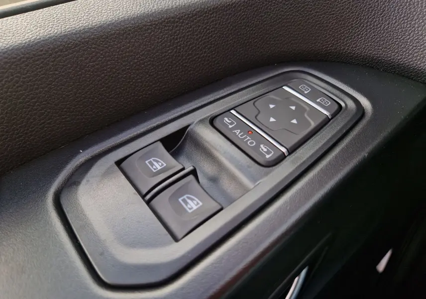 Gros plan sur les commandes de lève-vitres et réglage des rétroviseurs côté conducteur, plastique noir texturé.