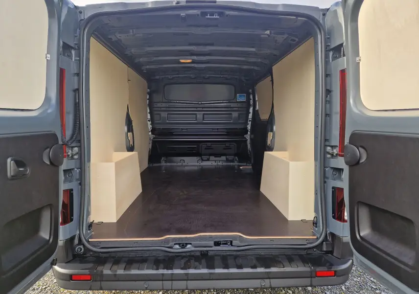 Vue arrière ouverte du Nissan Primastar gris urbain 2025, montrant l'aménagement bois intérieur du coffre spacieux.