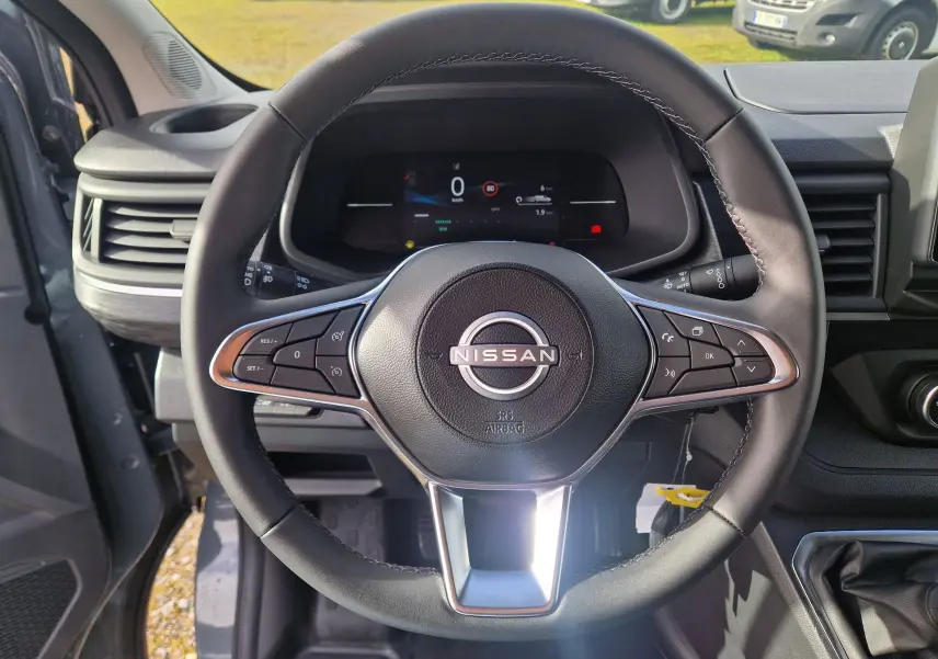 Vue rapprochée du volant noir du Nissan Primastar 2025 avec commandes intégrées et tableau de bord numérique.