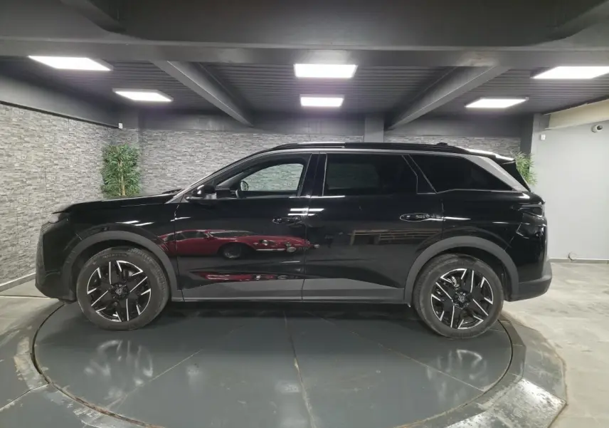 Vue de profil côté gauche d’un Peugeot 5008 noir 2025 avec jantes alliage 19 pouces et barres de toit noires.
