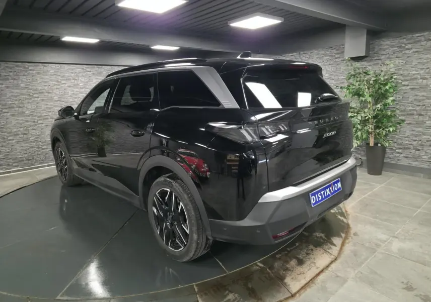 Vue 3/4 arrière droit d’un Peugeot 5008 noir brillant avec jantes alliage noires et vitres teintées en intérieur showroom.