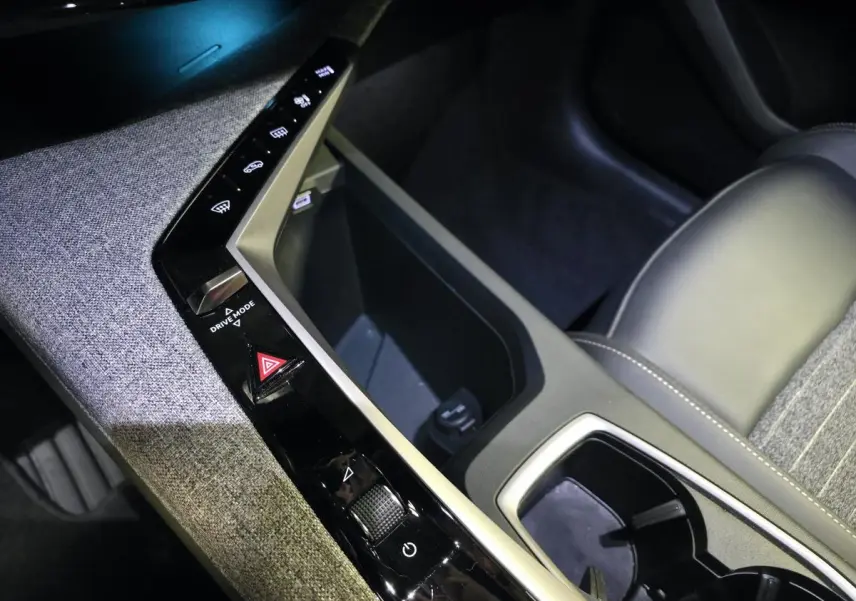 Détail de la console centrale avec commandes tactiles et rangement, sellerie tissu gris et cuir noir du Peugeot 5008 hybride 2025.